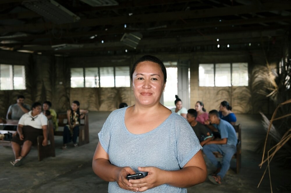 Woman smiles at the camera, people are seated at tables rows in the background.