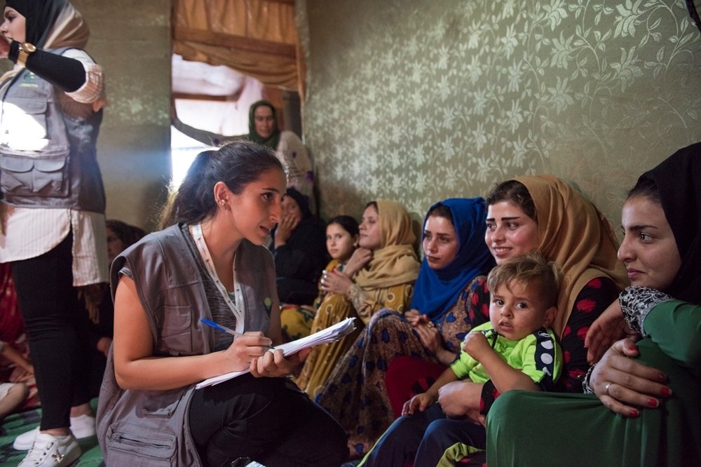 A youth worker with a clip board records answers from Syrian refugee women.