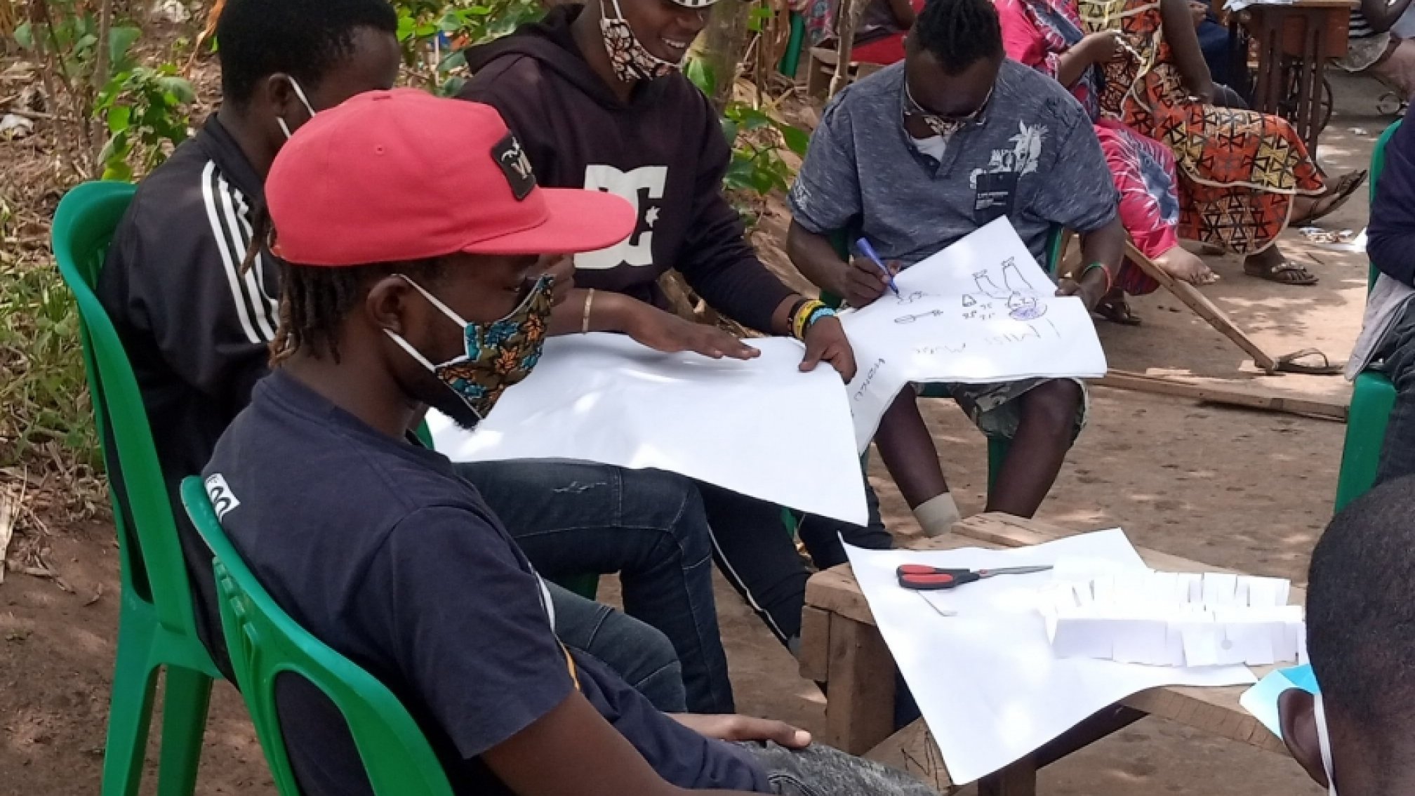 A group of young masculine people sit in a circle reading documents.
