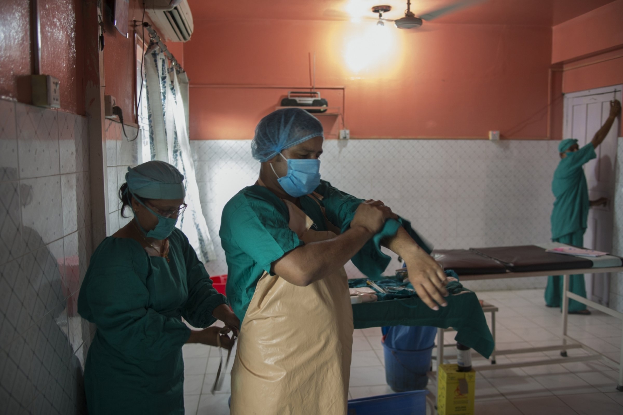 Doctor has an apron tied around their waste while washing their arms, up to the elbow.